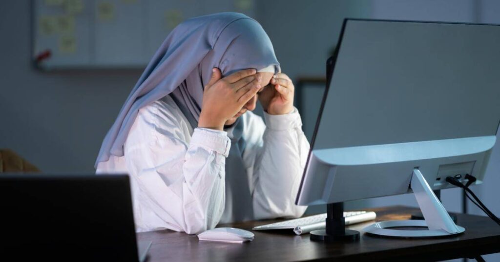 woman sitting in front of monitor with head in hands