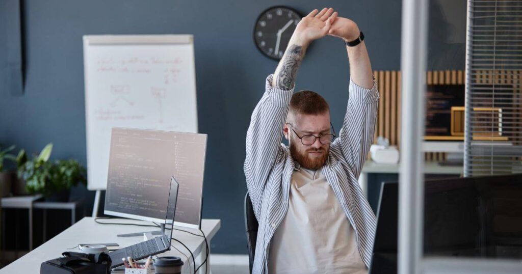 tech worker stretching in front of laptop